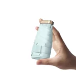 Petit parapluie léger et compact, couleur bleu clair, pratique et sécurisé avec sangle, idéal pour un transport facile.