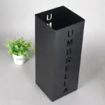 Porte-parapluies noir moderne marqué UMBRELLA, décoré avec une plante verte en pot, idéal pour organiser l'entrée avec style.