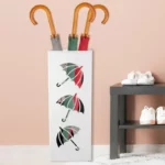 Porte parapluie en métal élégant, décoratif, avec parapluies colorés (gris, vert, rouge) près d'une table noire, chaussures blanches.