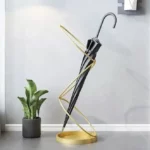 Porte-parapluie original doré avec parapluie noir, décoratif et moderne, accompagné d'une plante verte dans un intérieur design.