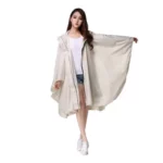 Poncho femme beige avec capuche et zip, imperméable léger mode, parfait pour la pluie, look casual avec t-shirt blanc et short denim.
