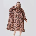 Femme souriante avec poncho long imperméable à motif léopard et capuche, parfait pour rester élégante et protégée sous la pluie.