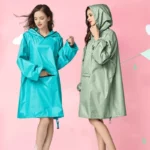 Deux femmes en ponchos colorés, turquoise et vert, sur fond rose, représentant des vêtements modernes pour affronter la pluie.