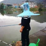 Homme pêchant près de l'eau, équipé d'un chapeau parapluie pliant, parfait pour se protéger de la pluie en extérieur.