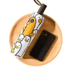 Parapluie rigolo coloré motif canard sur plateau bois, accessoire original pour égayer les journées pluvieuses.