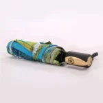 Parapluie automatique plié vert et bleu, léger et pratique, design élégant avec poignée noire et dorée, parfait pour tous les styles.