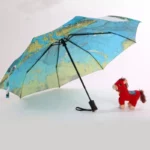 Parapluie automatique léger avec design carte du monde, parfait pour voyager, accompagné d'une peluche cheval rouge adorable.