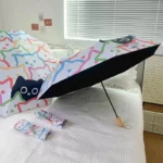 Parapluie automatique résistant avec motifs de chats colorés, ouvert et plié sur un lit blanc, accompagné de housses assorties.