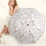 Parapluie pliable femme élégant avec motif floral, modèle assise en tenue décontractée, accessoire de mode pratique et stylé.