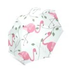 Parapluie flamant rose avec motifs tropicaux et feuillage vert sur fond blanc, idéal pour des journées de pluie stylées et joyeuses