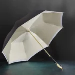 Parapluie homme luxe élégant, structure dorée, fond crème, ouvert sur fond sombre, accessoire haut de gamme pour homme raffiné.