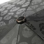 Parapluie homme robuste noir avec motif crânes, focus sur la base et coutures, design élégant et résistant des collections.