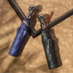 Parapluies homme robustes, design élégant, bleu et noir avec poignées crâne, accessoire tendance sur fond beige texturé.