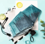 Parapluie pliable imperméable avec motifs dégradés bleu-gris, tranches de citron, feuilles décoratives et fond coloré esthétique.