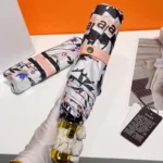 Parapluie luxe floral avec manche doré, design élégant et motifs raffinés, posé sur fond blanc aux côtés d'un autre parapluie.