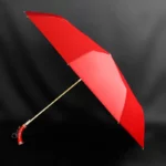 Parapluie luxe pliant rouge avec design élégant et poignée courbée, parfait pour accessoiriser avec style par tous les temps.
