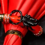 Parapluie luxe pliant rouge avec manche noir en forme de scorpion, détails raffinés et bijoux brillants, design unique et élégant.
