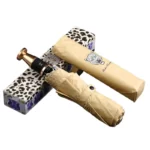 Parapluie luxe beige avec poignée dorée, design tête de léopard, emballage motif léopard, collection élégance et résistance.