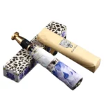 Parapluie luxe résistant pliable avec motif floral, posé sur boîtes à motifs animaliers, emballé dans papier kraft élégant.