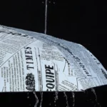 Parapluie automatique original avec motif pages de journal, protégeant de la pluie avec gouttes visibles sur fond noir.