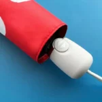 Parapluie original rouge avec motif blanc, partiellement ouvert, mécanisme d'ouverture visible, sur fond bleu lumineux.