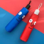 Parapluies originaux colorés, bleu et rouge, avec visages ludiques, design unique, fond dégradé vibrant. Idéal pour égayer vos jours de pluie!
