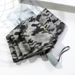 Parapluie pliant camouflage gris, compact et élégant, idéal pour la pluie, présenté sur fond blanc avec magazine en arrière-plan.