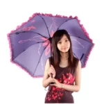 Parapluie vintage violet à motifs floraux avec bord festonné rose, élégant et pratique, porté par une femme dans un décor lumineux.