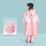 Poncho bébé coloré rose avec ailes blanches, motif fun, assorti à un sac à dos, idéal pour jours de pluie et looks joyeux.