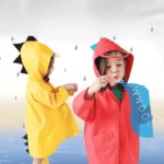 Poncho bébé dinosaure coloré : enfant heureux sous la pluie en poncho jaune à écailles, jouant avec des bulles et des gouttes d'eau.