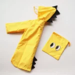 Poncho bébé dinosaure jaune imperméable avec capuche dentée, sac assorti, parfait pour enfants, style ludique et protection pluie.