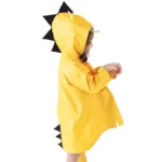 Poncho bébé dinosaure jaune à capuche avec piques noires, idéal pour jouer sous la pluie et protéger votre enfant avec style.