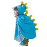 Enfant avec poncho bébé léger bleu à capuche pointes jaunes, bottes dinosaure vertes, jouant sous la pluie joyeusement.
