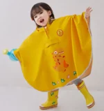 Enfant souriant avec poncho bébé jaune motif dinosaure, bottes assorties, jouant sous la pluie - idéal pour comfort et style enfant.