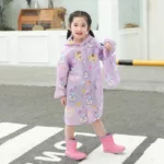 Poncho bébé à longues manches violet avec motifs de lapins, porté par une petite fille souriante en extérieur sur un chemin.