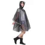 Femme souriante en poncho pluie transparent avec capuche, idéale pour [Collection], associée à des bottes noires tendance.