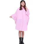 Femme souriante portant un poncho pluie rose avec capuche, debout avec bottes noires, idéal pour rester au sec avec style.