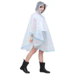 Femme avec poncho pluie coloré et motifs, capuche relevée, marchant sous la pluie avec bottes noires, style tendance et pratique.