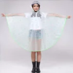 Femme souriante en poncho pluie transparent vert avec capuche, bras écartés, combinaison pratique et stylée contre la pluie.