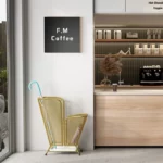 Porte-parapluie métallique doré avec parapluies colorés, décor moderne et panneau F.M Coffee dans un espace épuré.