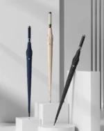 Parapluies chics en bleu marine, beige et noir avec design moderne et poignées stylées, exposés sur des socles blancs.