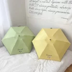 Mini parapluies de poche colorés, vert 'amazed' et jaune 'happiness', posés sur un lit au fond de drap blanc, design compact.