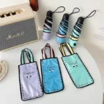 Mini parapluies pliables colorés avec housses amusantes (Happiness, Angry, Amazed), posés sur une table moderne, rétro en arrière.