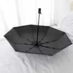 Parapluie anglais automatique noir ouvert, élégant et robuste, exposé sur un lit, montrant sa structure et son design raffiné.
