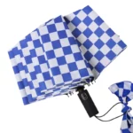 Parapluie anglais femme bleu et blanc à motifs damier, ouvert avec poignée noire élégante et attache pratique pour le fermer.