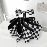 Parapluie anglais femme élégant au motif checkered noir et blanc, avec nœud en tissu, posé ouvert sur un lit raffiné.
