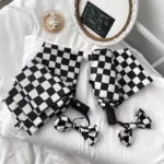 Parapluie anglais femme élégant, motif damier noir et blanc avec nœuds raffinés, posé sur un lit blanc avec une illustration.