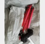 Parapluie de pêche noir avec motifs, plié, accompagné de piquets rouges et d'une housse grise pour rangement pratique.