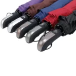 Parapluies tempête légers colorés avec poignées automatiques, disponibles en violet, marron, bleu, rouge et noir, alignés en rangée.