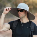 Homme avec chapeau de pluie large bord anti-UV imperméable, lunettes de soleil et sac à dos, parfait pour activités extérieures.